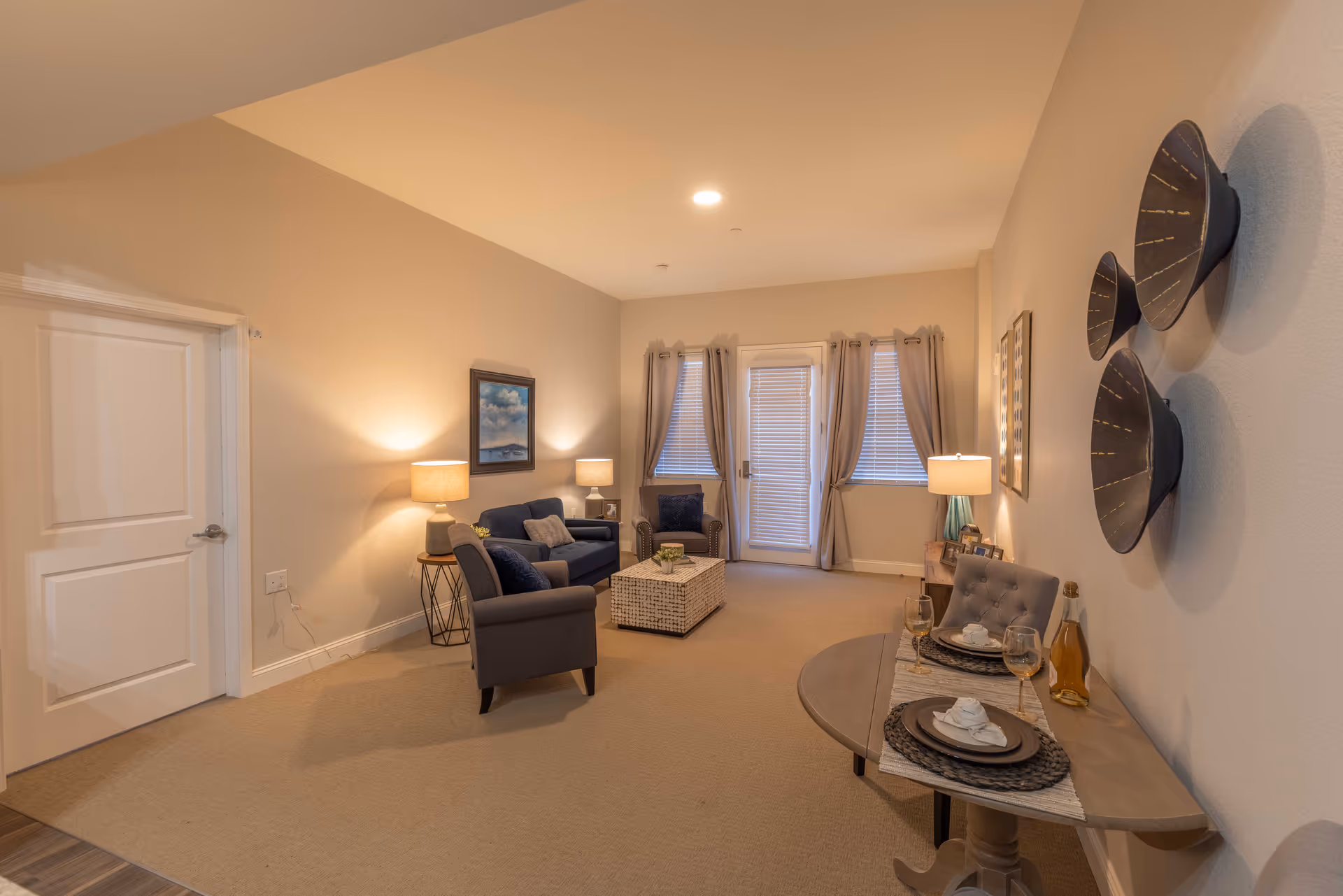 A cozy furnished living room with sofas and armchairs, a central ottoman, lamps, and decorative wall art.