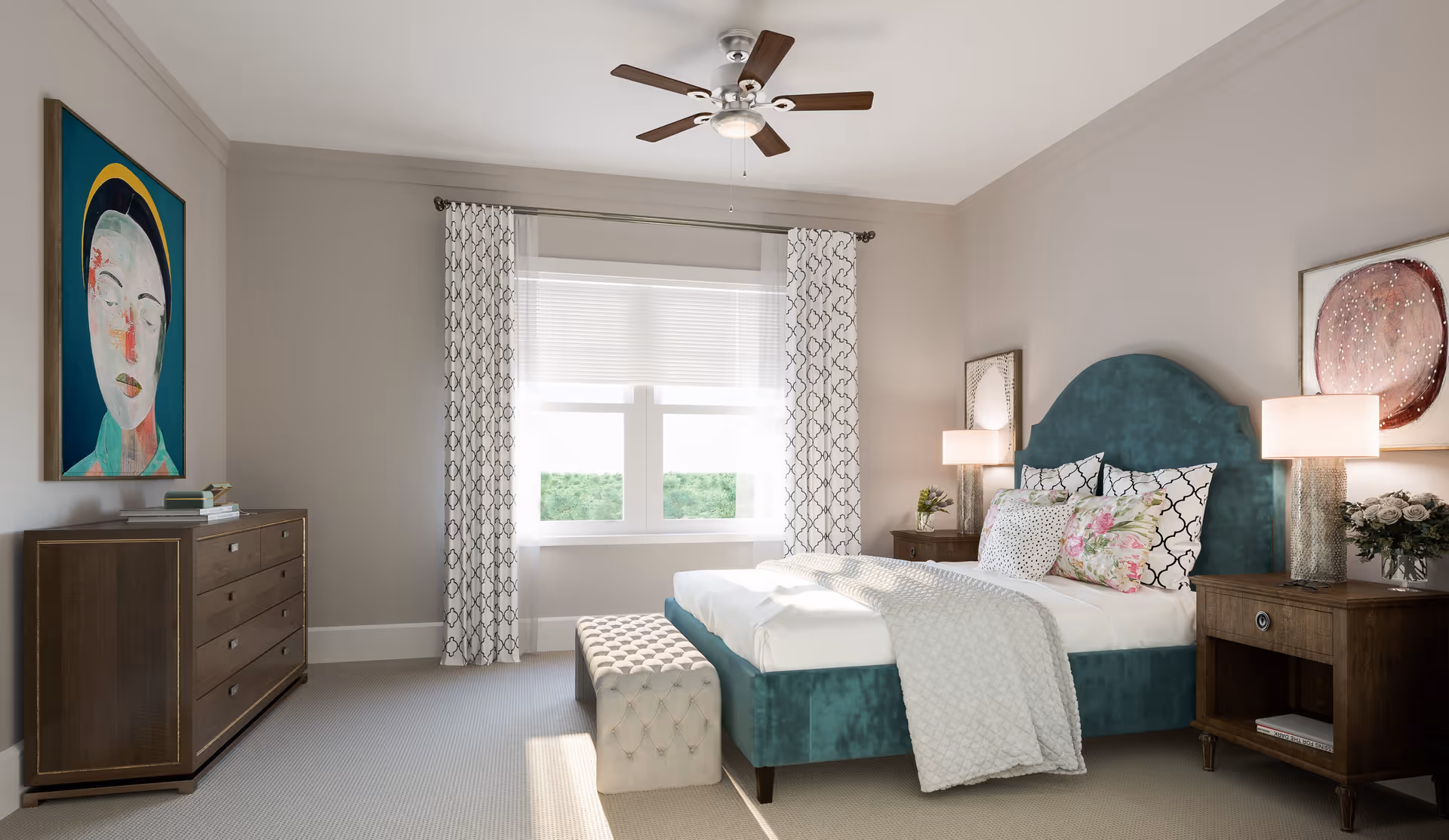 A bright and airy bedroom with a teal upholstered bed, white bedding, and decorative pillows. There are two wooden nightstands with lamps on either side of the bed, a wooden dresser with books and a colorful portrait hanging above it, and a window with patterned curtains letting in natural light. A ceiling fan with lights is mounted on the ceiling.