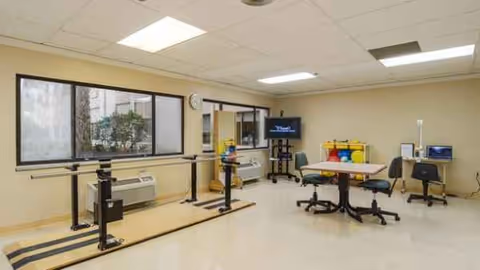 Rehabilitation therapy room with parallel bars, equipment, and a person near a doorway.