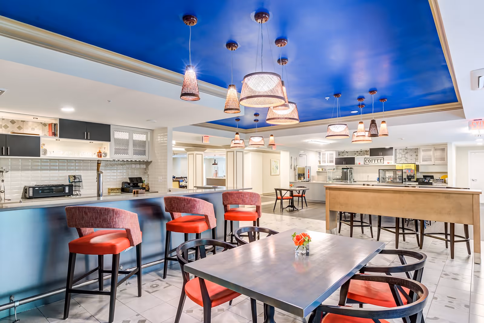 Bright communal dining and café area with a blue ceiling, pendant lights, bar seating and tables.