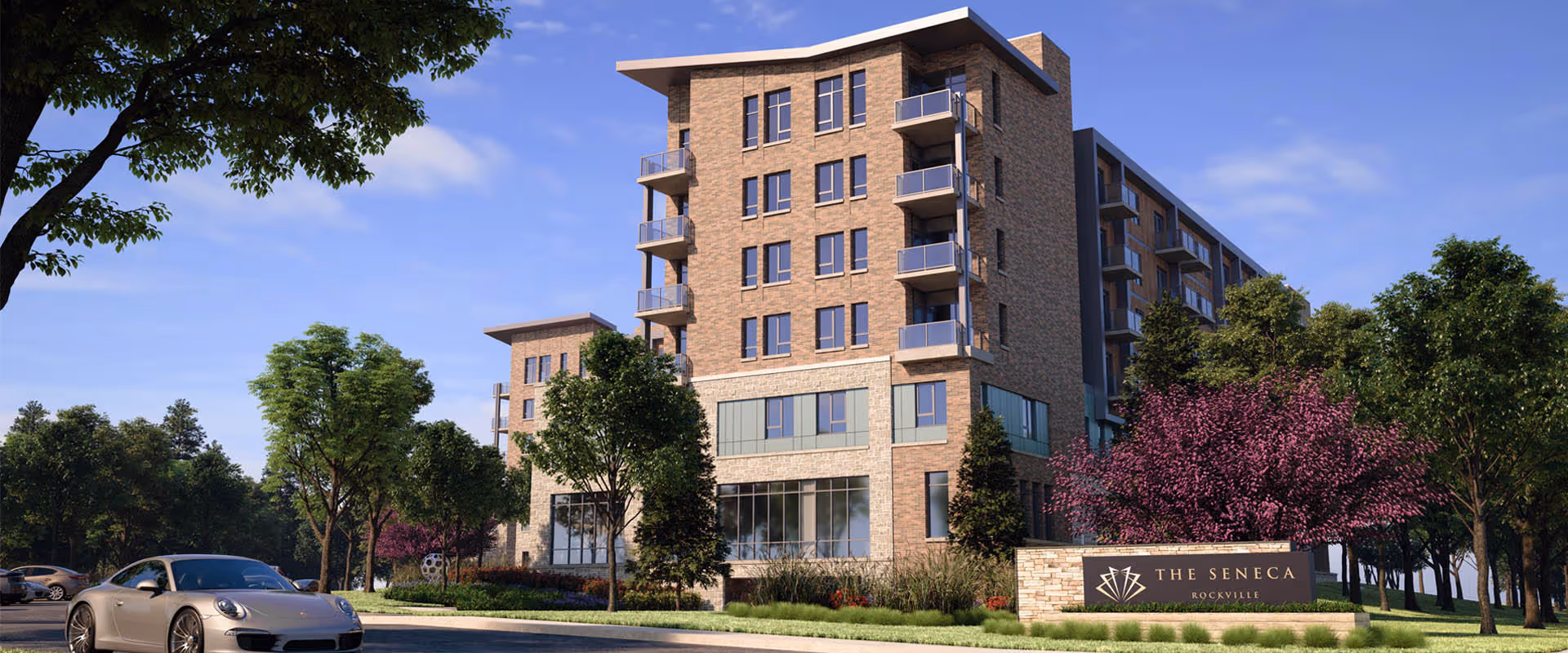 Exterior view of The Seneca Rockville, a multi-story senior living facility with balconies, surrounded by trees and landscaping, under a clear blue sky. A silver car is parked on the driveway in front of the building.