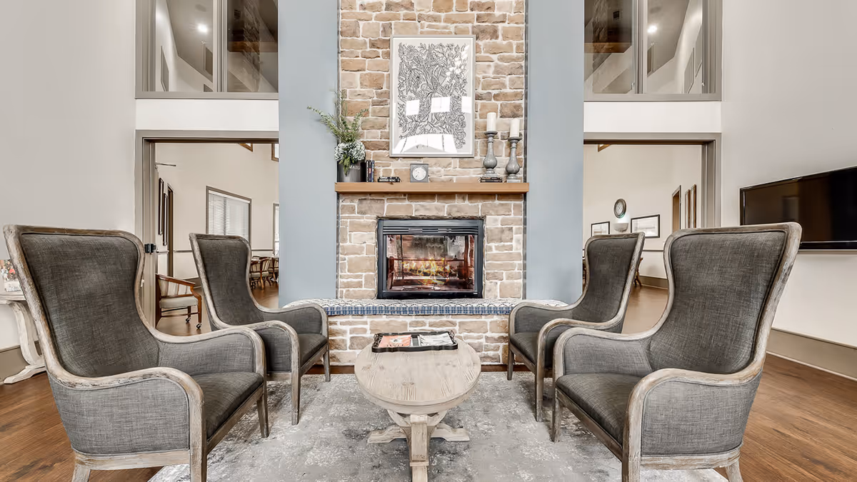 Common sitting area with four upholstered armchairs around a wooden coffee table facing a stone fireplace and mantel.