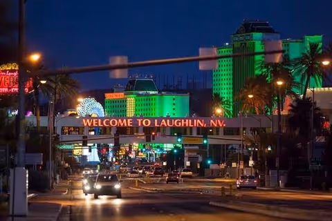 Nighttime view of a busy street with an illuminated 'WELCOME TO LAUGHLIN, NV' overhead sign and brightly lit buildings in the background.