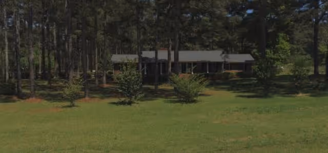 A single-story care home exterior with a green lawn and tall trees.