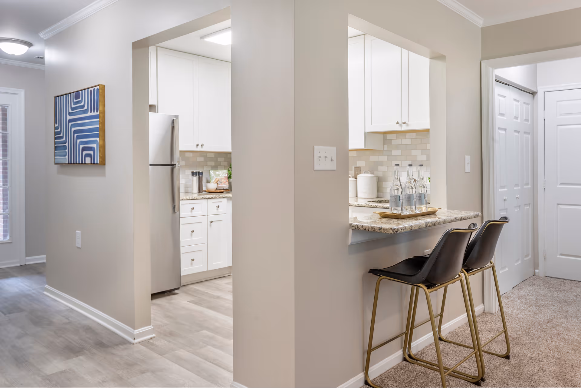 Bright, modern kitchen with white cabinets, stainless fridge, and granite counter.