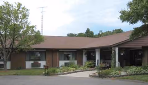 Single-story brick senior living facility exterior with walkway, entrance, and landscaping.