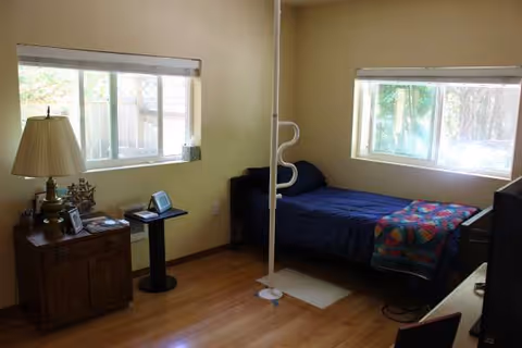 A small bedroom with a single bed, nightstand, lamp, and a white vertical support pole.