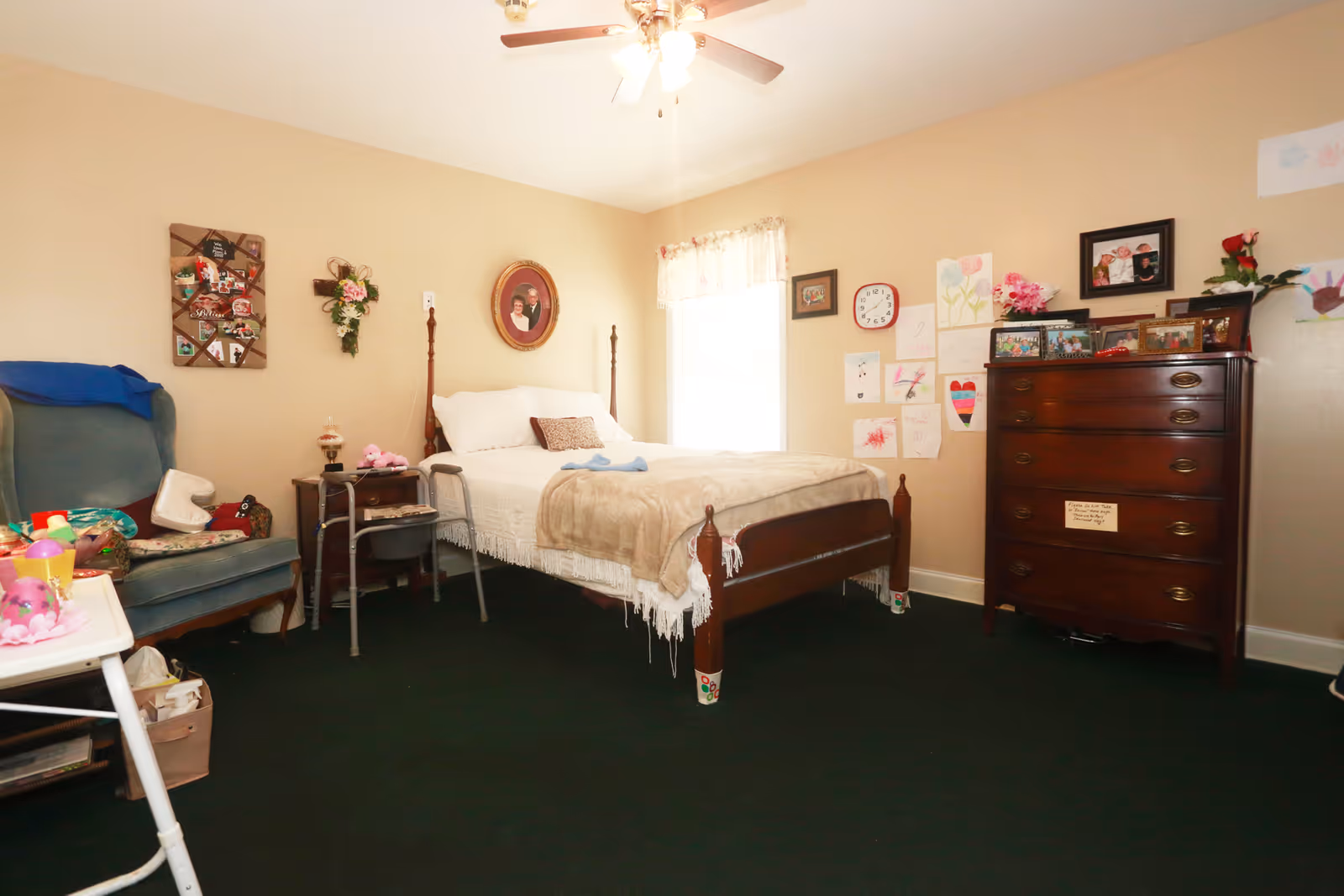 A cozy furnished bedroom with a made bed, wooden dresser, armchair, bedside table and artwork on the walls.