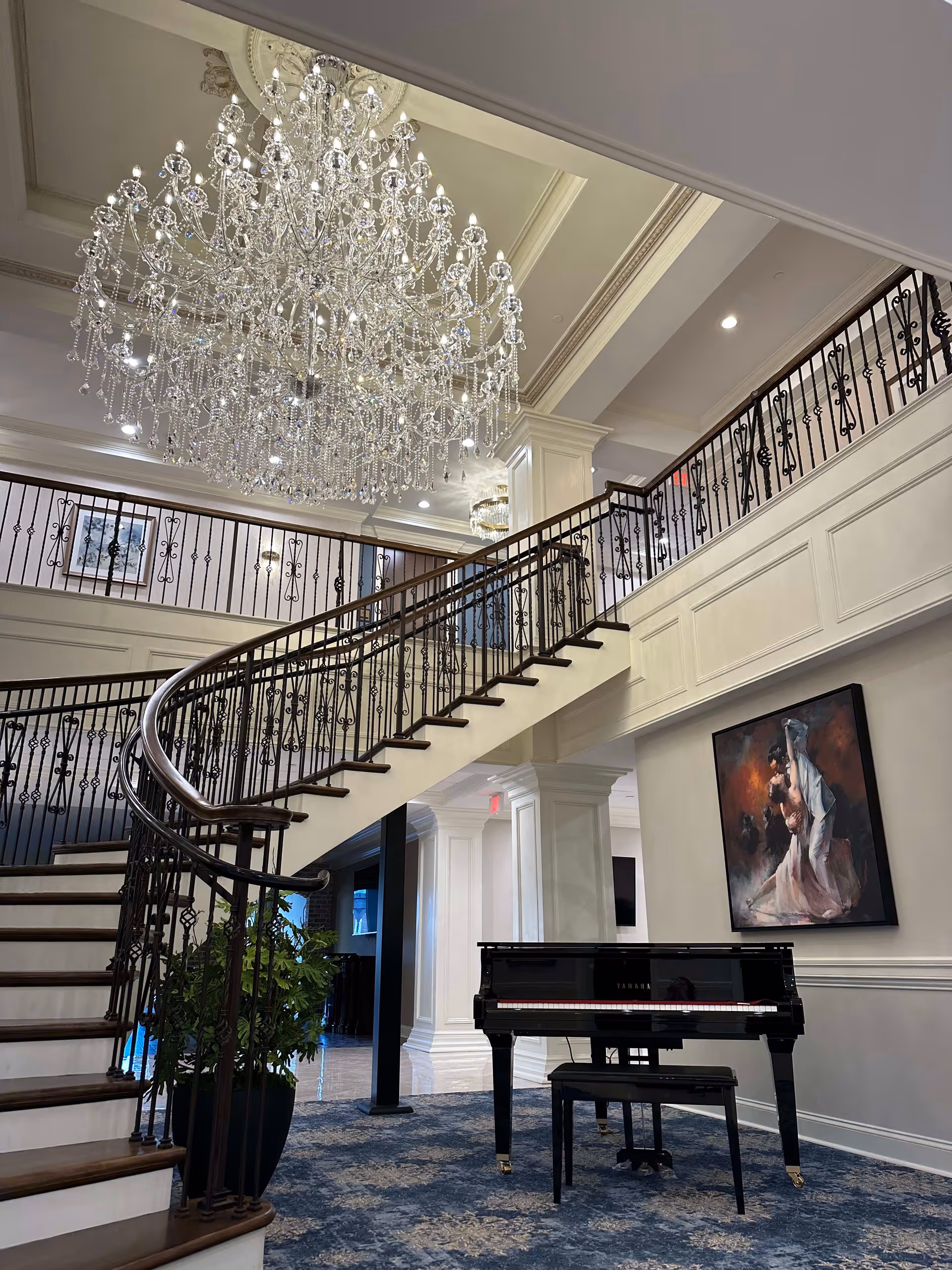 Elegant two-story foyer with a sweeping curved staircase, large crystal chandelier, and a black grand piano.
