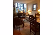 Well-lit living room with a sofa, armchair, coffee table and a dining table with chairs near a large window.