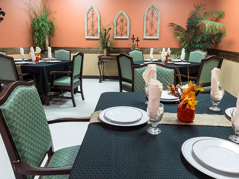 A dining room with several tables set with plates, glasses, folded napkins and small floral centerpieces.