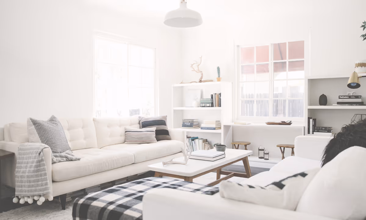 Bright modern living room with white sofas, a coffee table, shelving and large windows.
