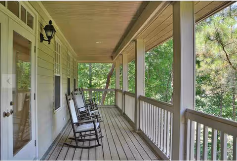 Covered porch with rocking chairs along railing overlooking trees.