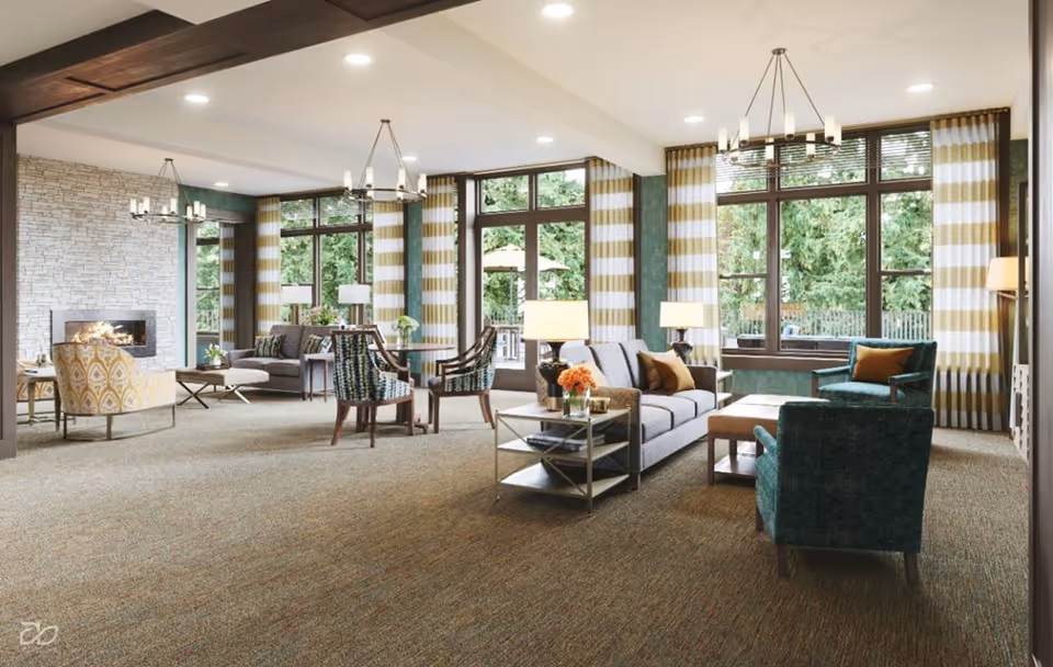 Spacious, well-lit senior living common room with sofas, armchairs, large windows, and a fireplace.