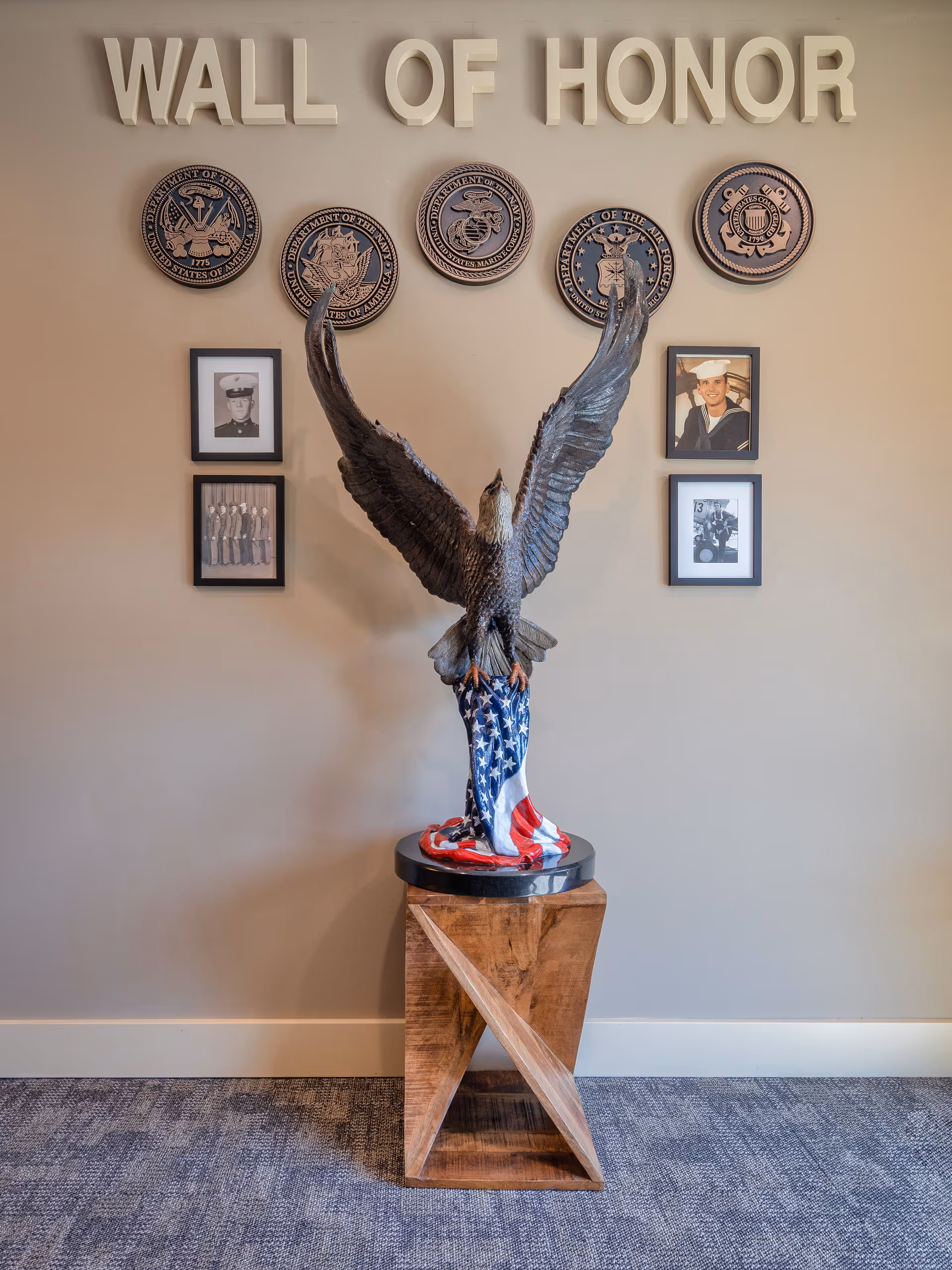 Indoor 'Wall of Honor' display with a large eagle statue draped in an American flag beneath military seals and framed photos.