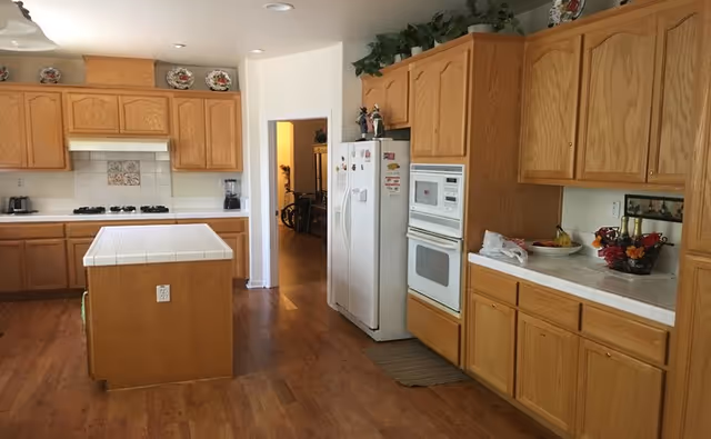 Spacious kitchen with oak cabinets, a central tiled island, white refrigerator and built-in oven, and hardwood floors.