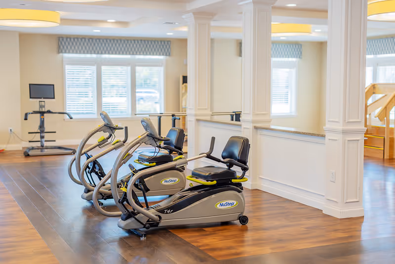 Bright interior exercise room with three NuStep recumbent exercise bikes on a wood floor near large windows.