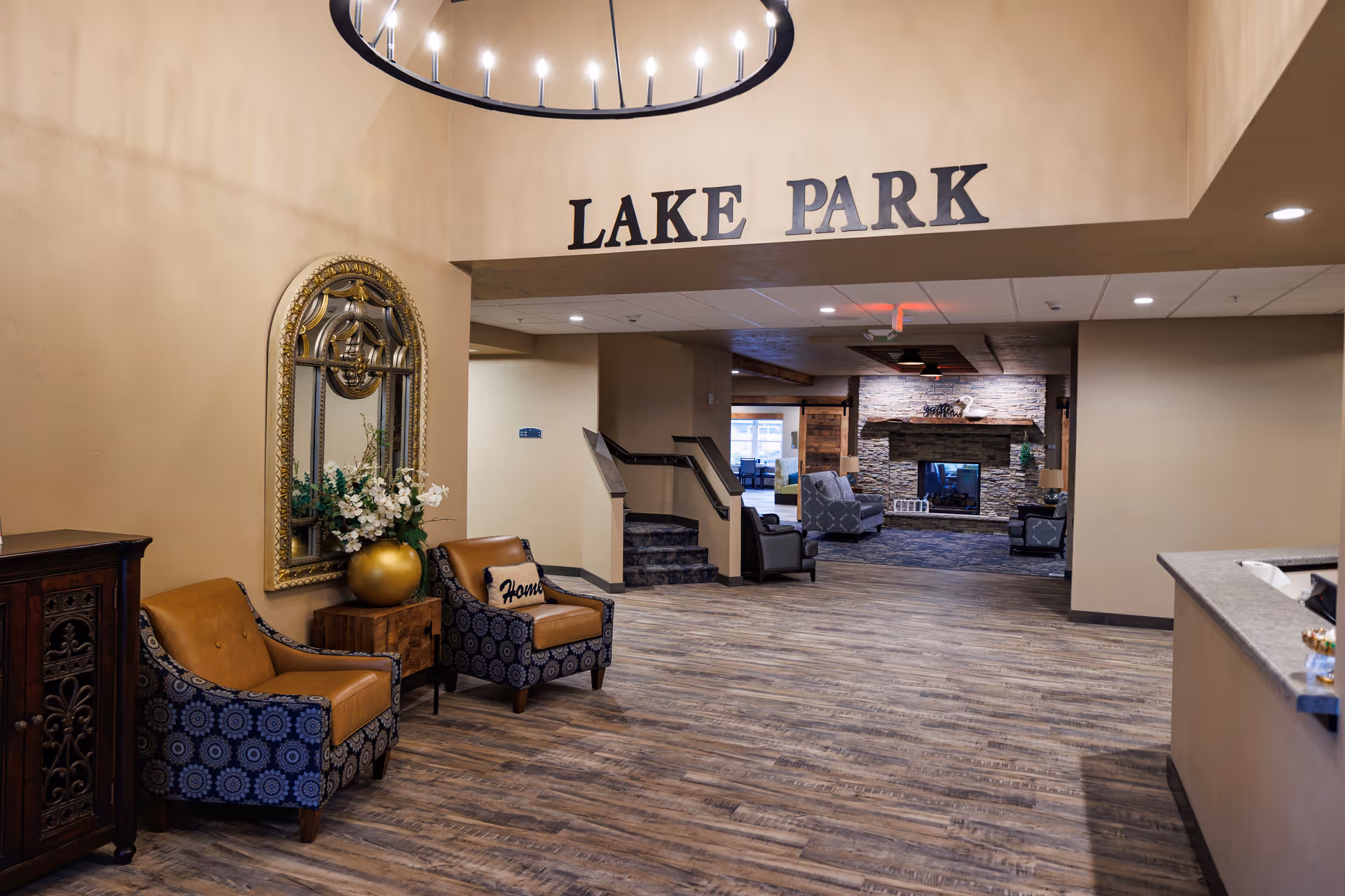 Interior lobby with seating, decorative mirror and flowers, and a distant fireplace beneath a large 'LAKE PARK' sign.