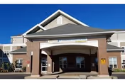 Front entrance of a brick-and-beige nursing home building with a covered porte-cochère beneath a clear blue sky.