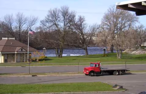 Exterior scene with a red flatbed truck on a street near a grassy area and trees.