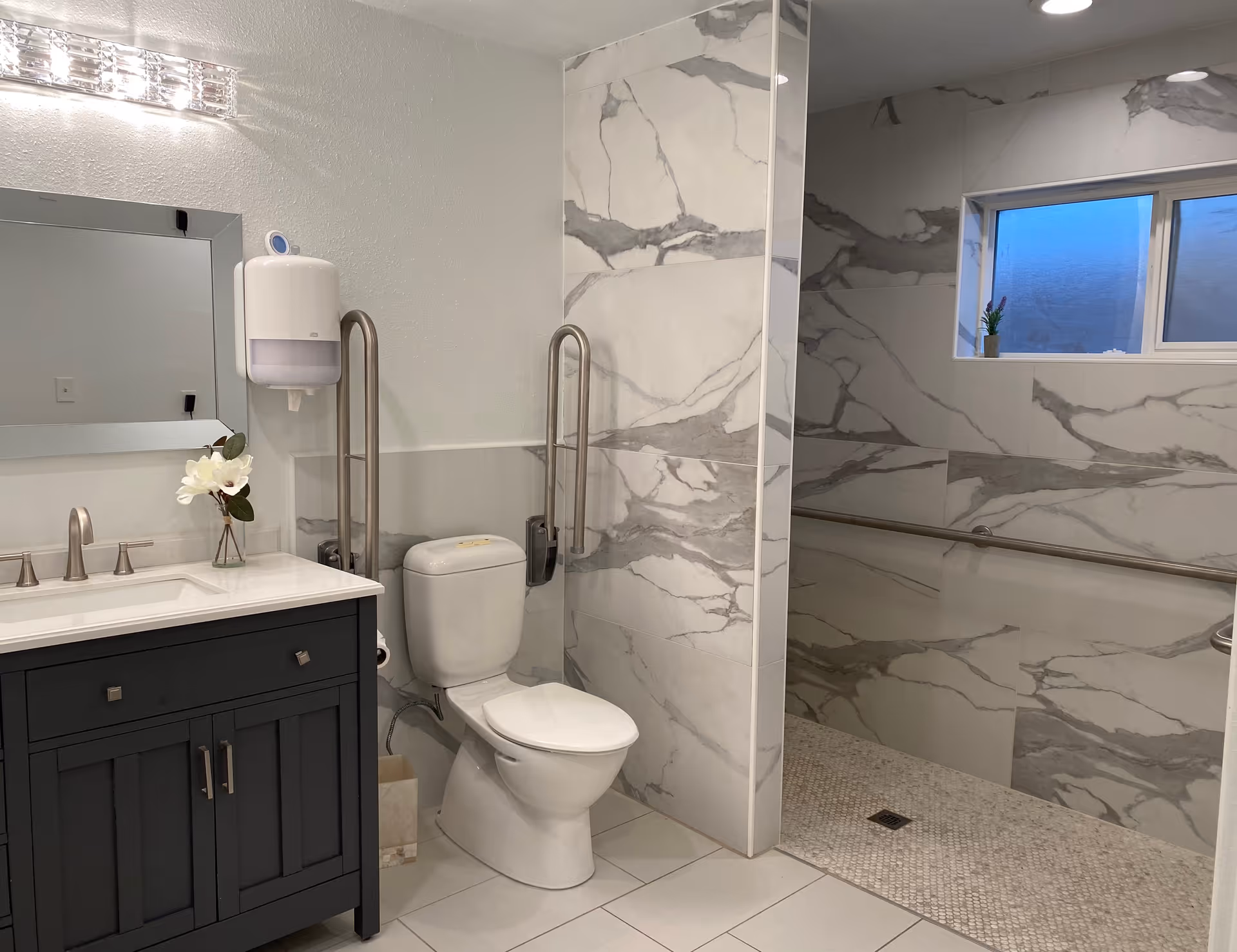 Modern accessible bathroom featuring a vanity with mirror, a toilet flanked by grab bars, and a walk-in tiled shower.