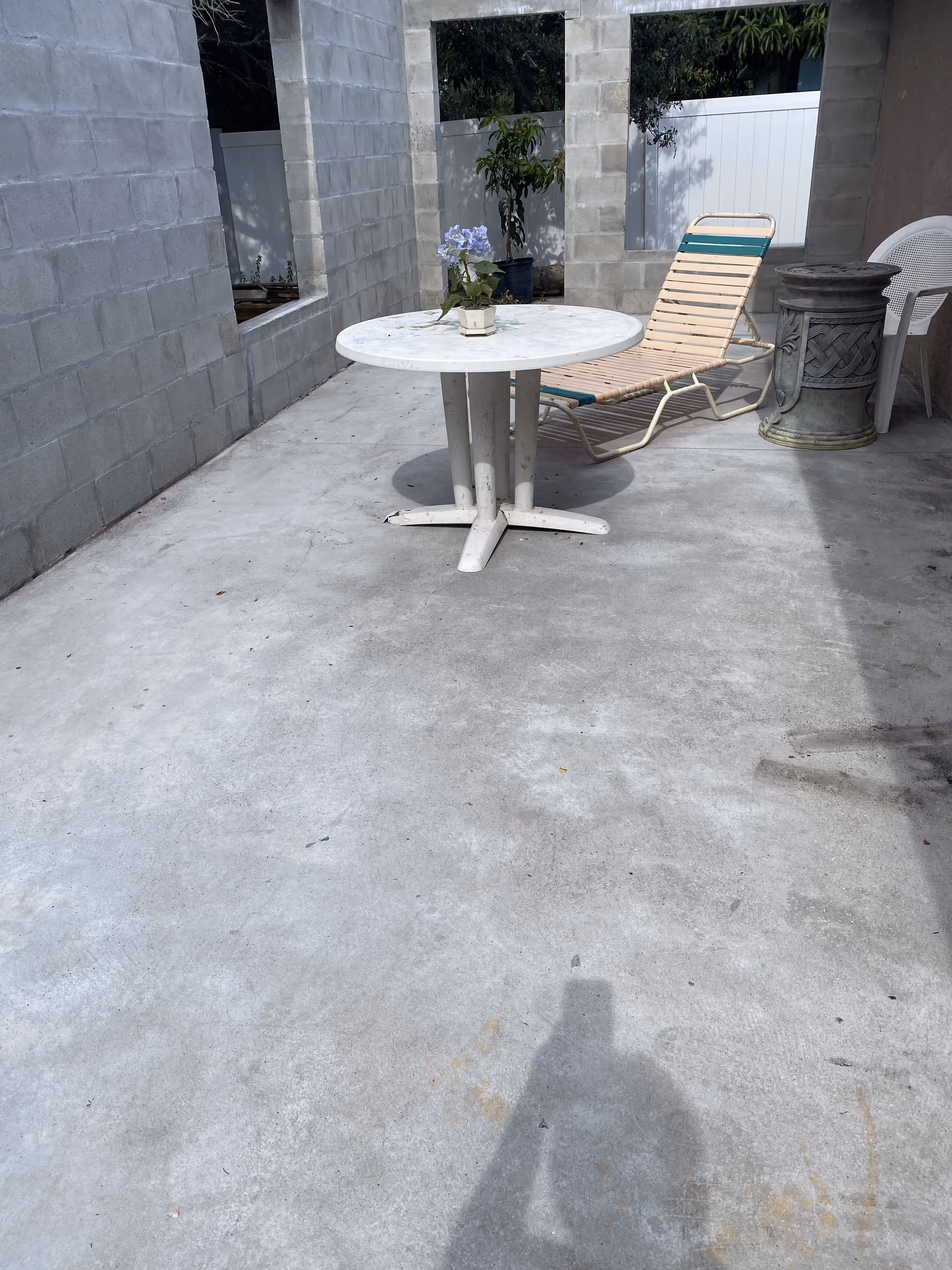 Concrete patio with a round white table holding a potted plant and a lounge chair beside cinderblock walls.