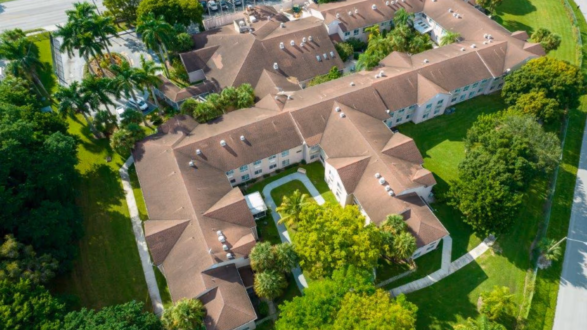 Aerial view of a large U-shaped nursing facility with brown roofs surrounded by lawns, trees, and walkways.