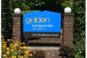 Blue sign reading Golden Living Center Mt. Lebanon between brick pillars and surrounding flowers.