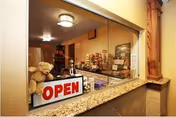 Reception window with a granite counter displaying an 'OPEN' sign, a teddy bear, and decorative items inside a senior living facility.