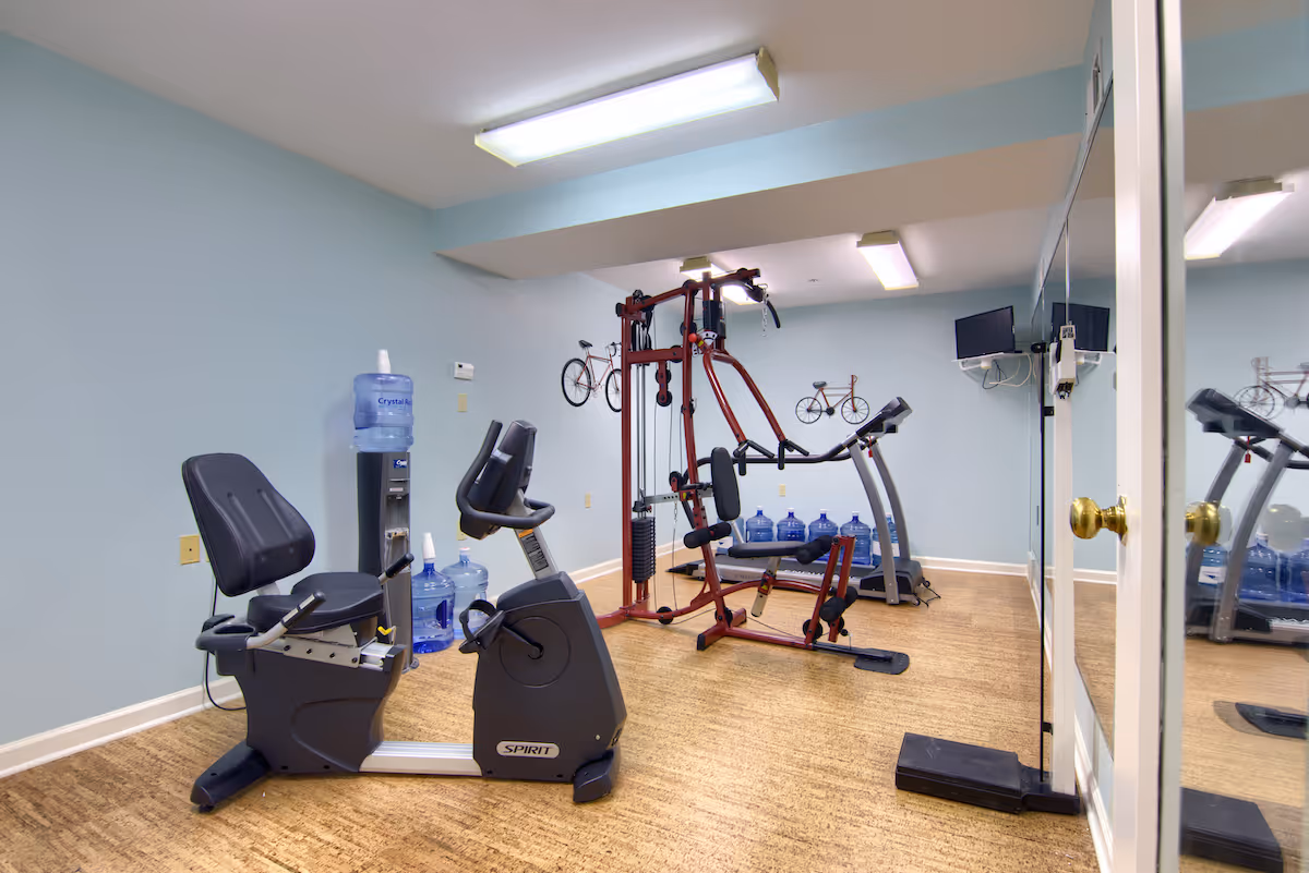 Small fitness room with a recumbent exercise bike, multi-station weight machine, treadmill, water cooler and mirrored wall.