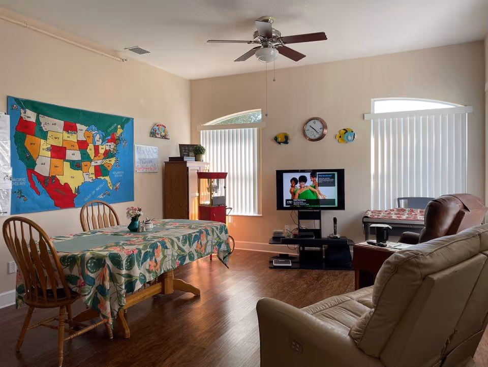 Interior senior living common area with table, map, TV, and sofa.