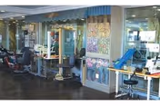 Interior view of a salon area with multiple barber chairs and workstations equipped with mirrors and hairdressing tools. The space has a polished floor and decorative wall panels with floral artwork.