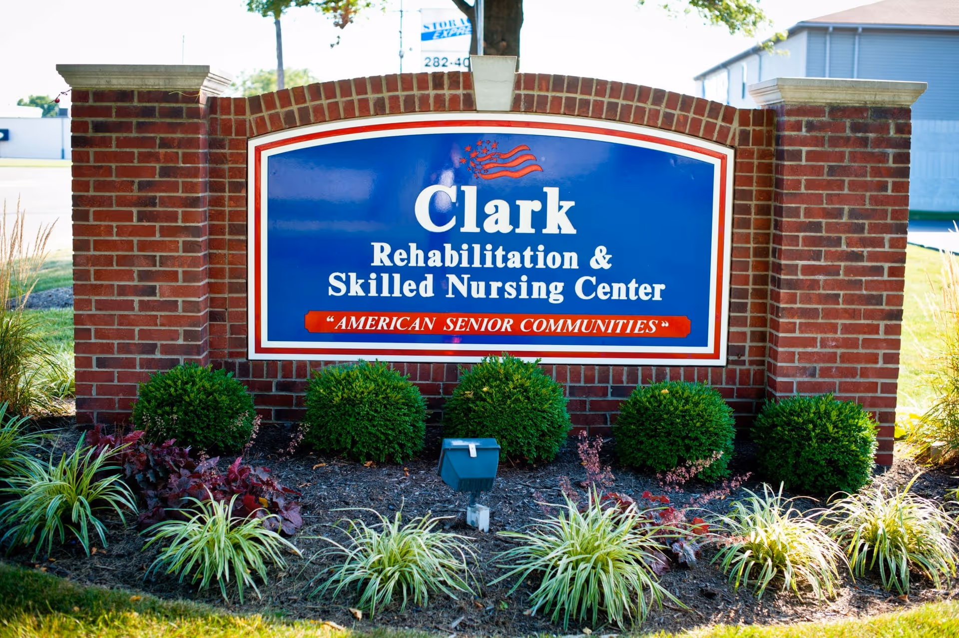 Brick monument sign reading "Clark Rehabilitation & Skilled Nursing Center" set in a landscaped bed in front of the facility.