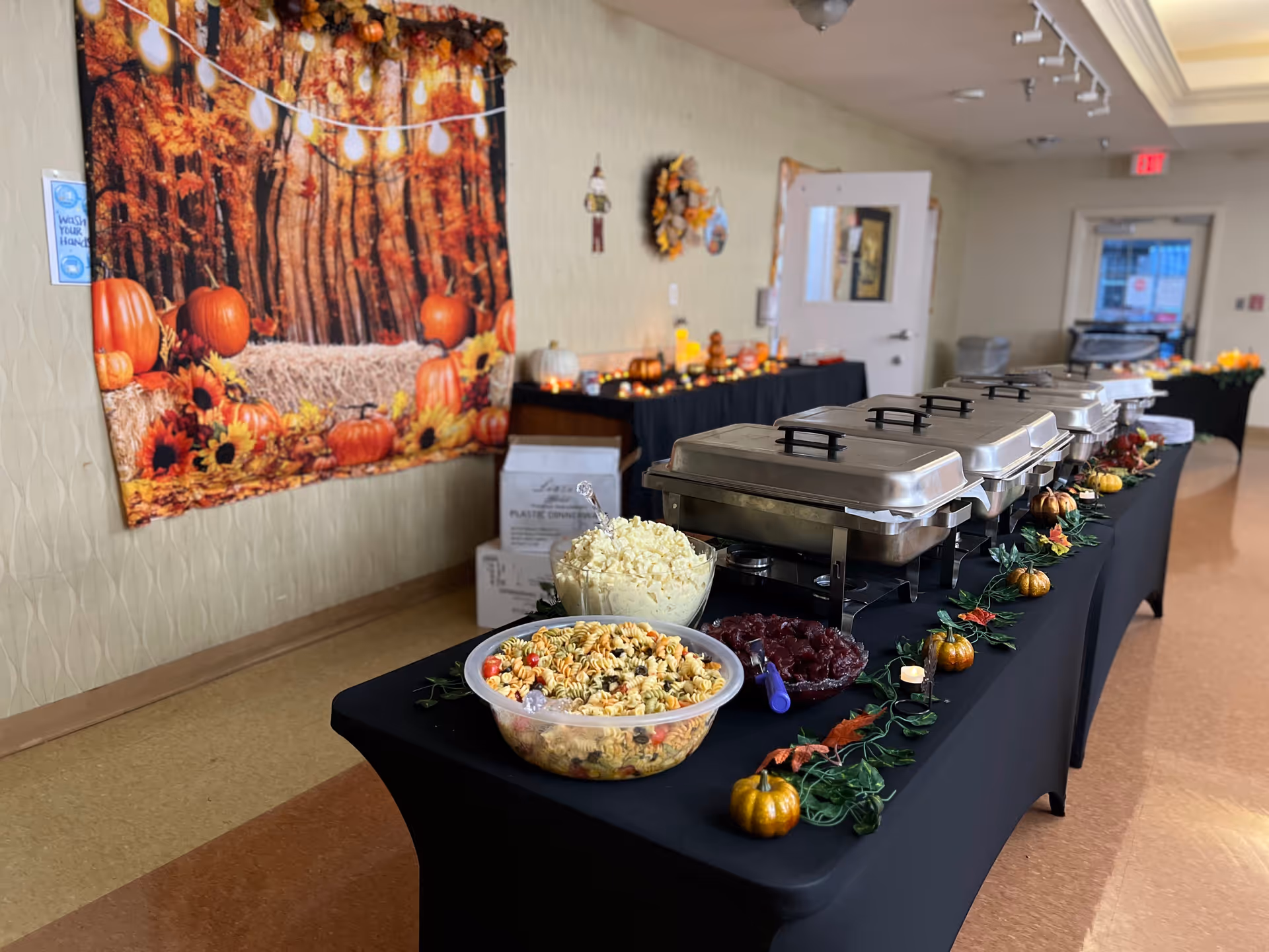 Buffet table with covered chafing dishes, bowls of salad and fall decorations set up in a decorated dining area.