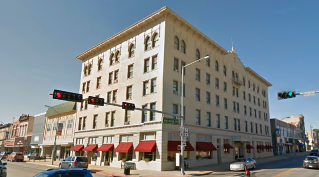 Corner street view of a large building with red awning storefronts and traffic.