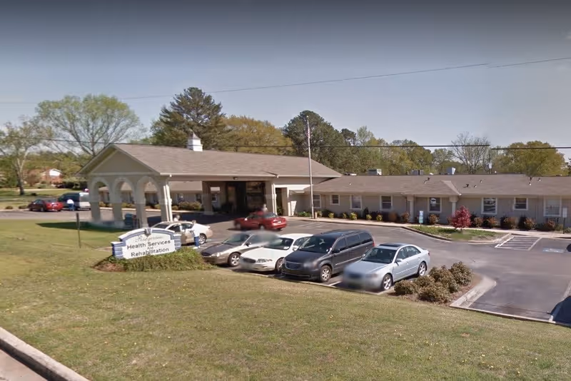 Front exterior of a single-story health services building with a covered entrance, sign and parked cars in the lot.
