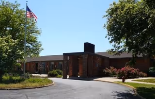Brick exterior of a senior living center with a flag, trees, and curved driveway.