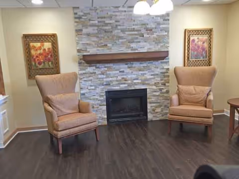 Two beige armchairs flank a stone fireplace with a wooden mantel in a cozy living room.