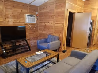 Wood-paneled living room with a sofa, armchair, coffee table, flat-screen TV, and a wall-mounted air conditioner.