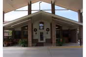 Covered main entrance of a brick nursing home with a porte-cochere, double glass doors, brick columns, potted plants, and wreaths.