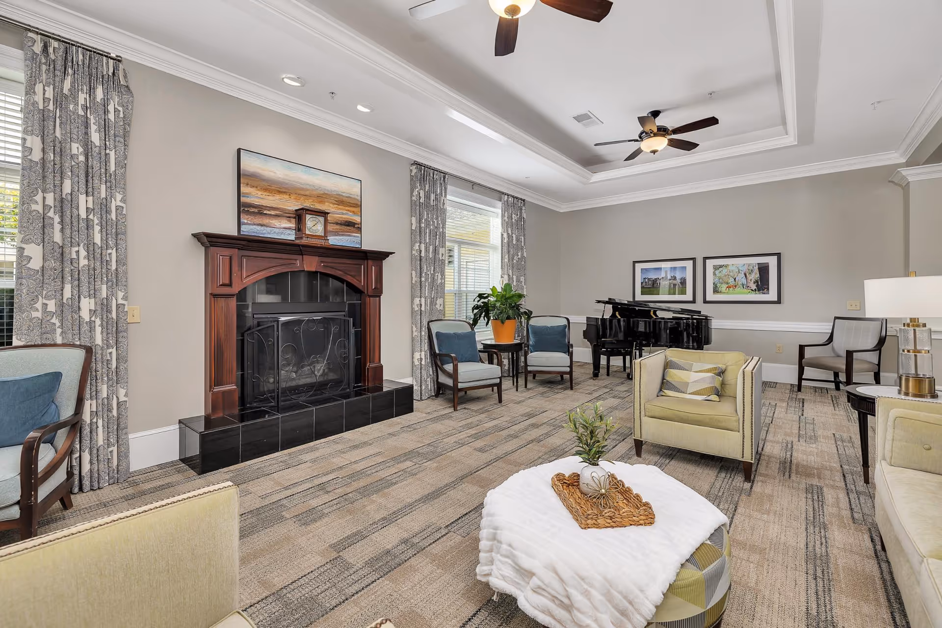 Bright communal lounge with a fireplace, multiple armchairs and sofas, a grand piano, and a coffered ceiling.