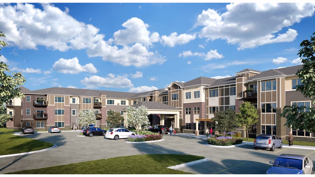 Exterior view of a large, modern three-story senior living facility with multiple windows and balconies. Several cars are parked in front of the building near a covered entrance. The sky is blue with scattered clouds, and there are trees and landscaped greenery around the parking area.