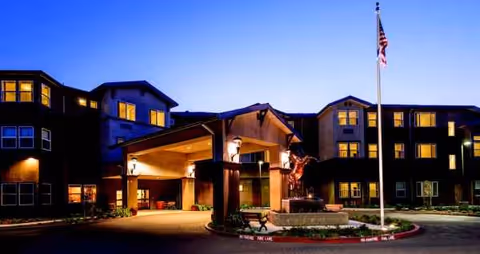 Exterior view of Carlton Senior Living Davis with illuminated entrance and flagpole at dusk.