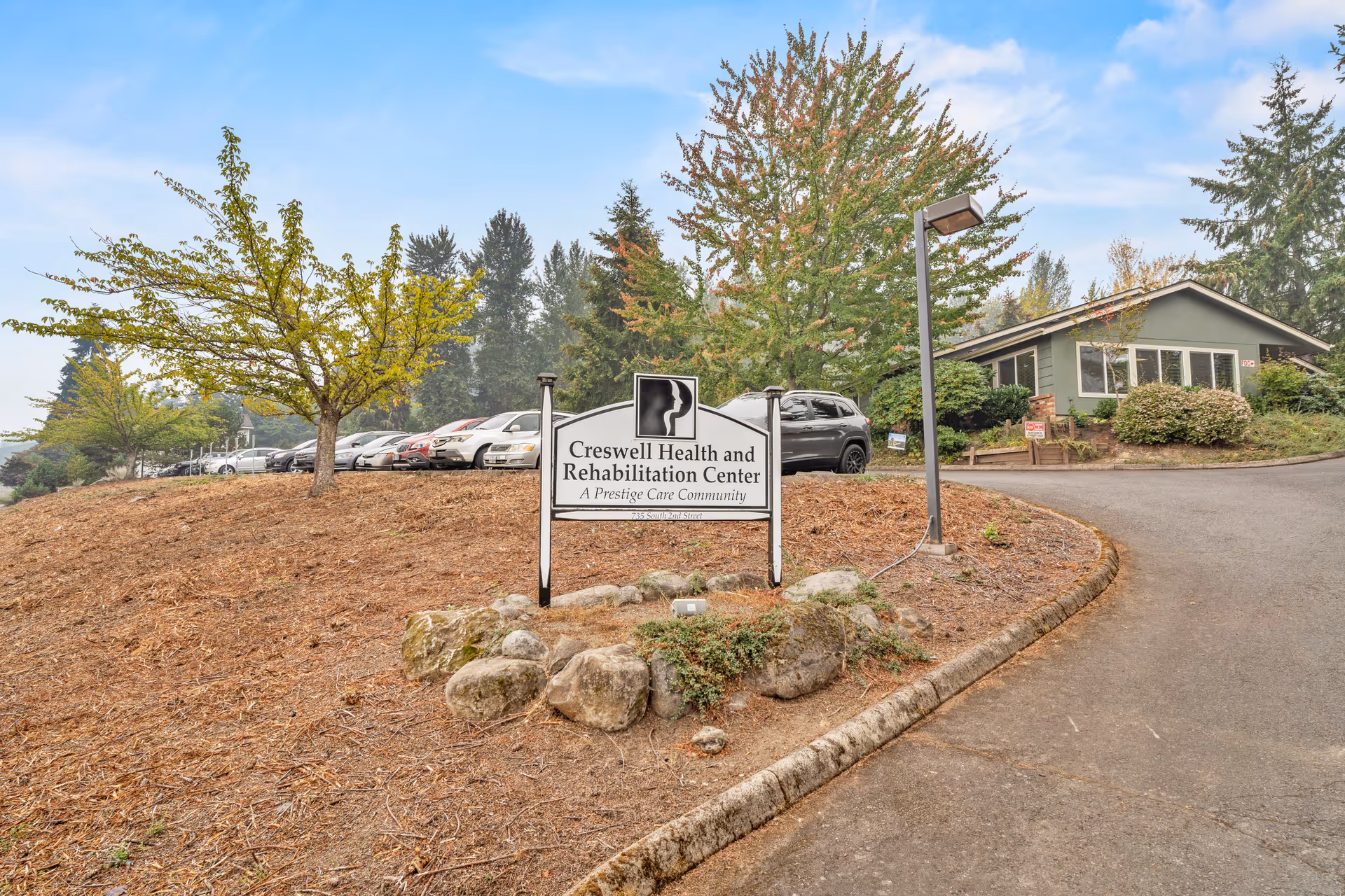 Entrance sign reading 'Creswell Health and Rehabilitation Center' in front of a parking area, trees, and a single-story building.