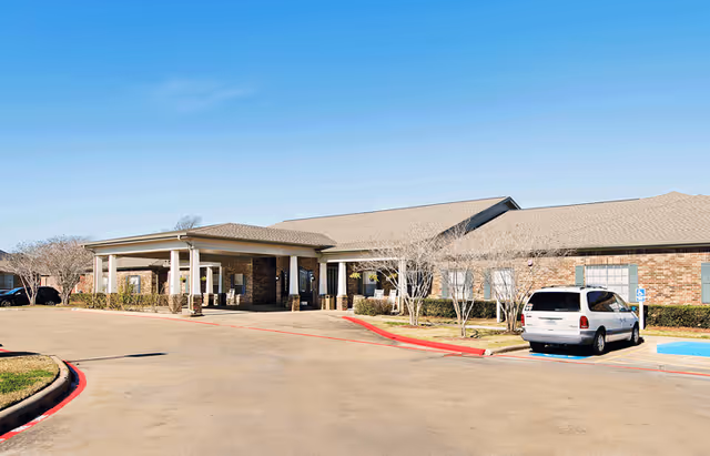 Single-story brick senior living facility with a covered entrance, parking area, and a parked van.