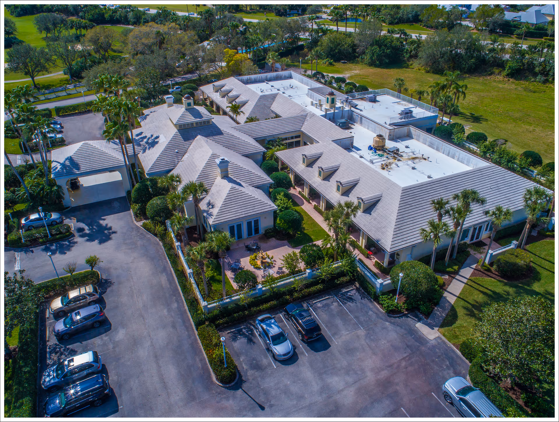 Aerial view of a one-story senior living facility with multiple pitched roofs, a landscaped courtyard and parked cars.