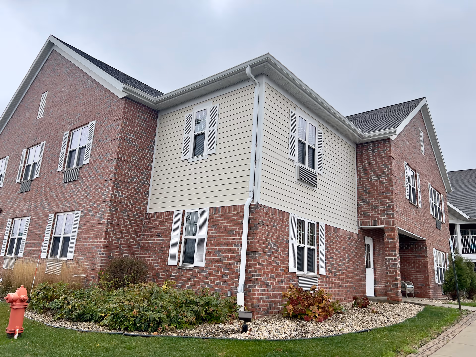 Exterior view of a two-story brick-and-siding assisted living building with windows, landscaping, and a red fire hydrant.