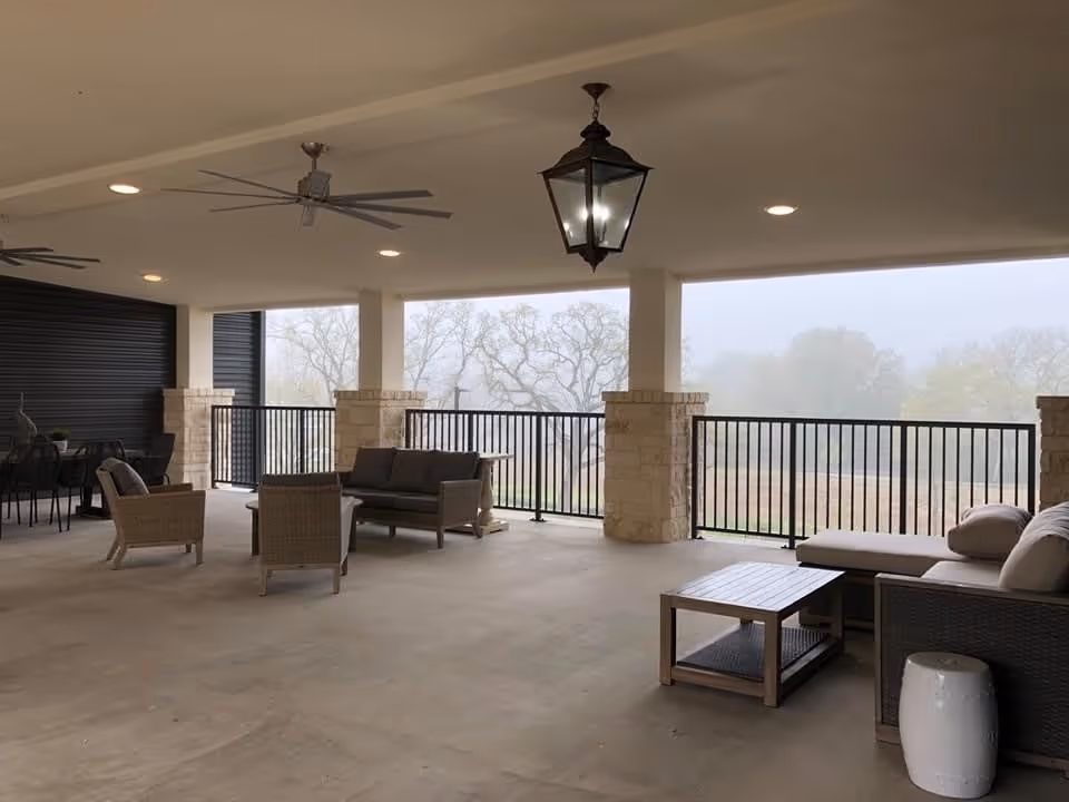Covered outdoor patio with sofas, chairs, tables, ceiling fans and a hanging lantern overlooking foggy trees.