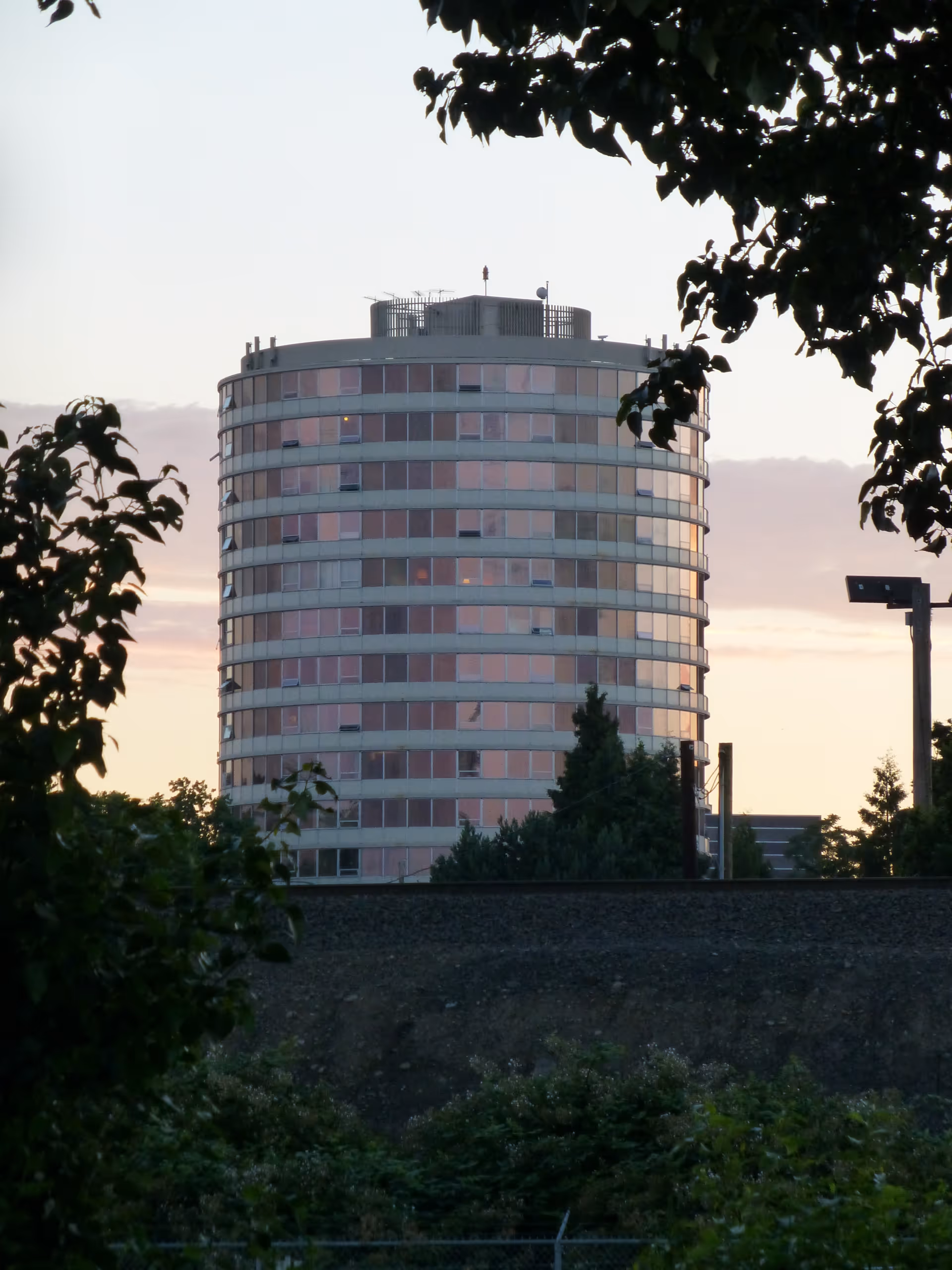 Round multi-story apartment tower framed by trees against a dusk sky.