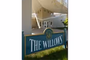 Outdoor view of the entrance area of a facility named The Willows, featuring a large sign with the facility name in front of a covered walkway and building exterior.
